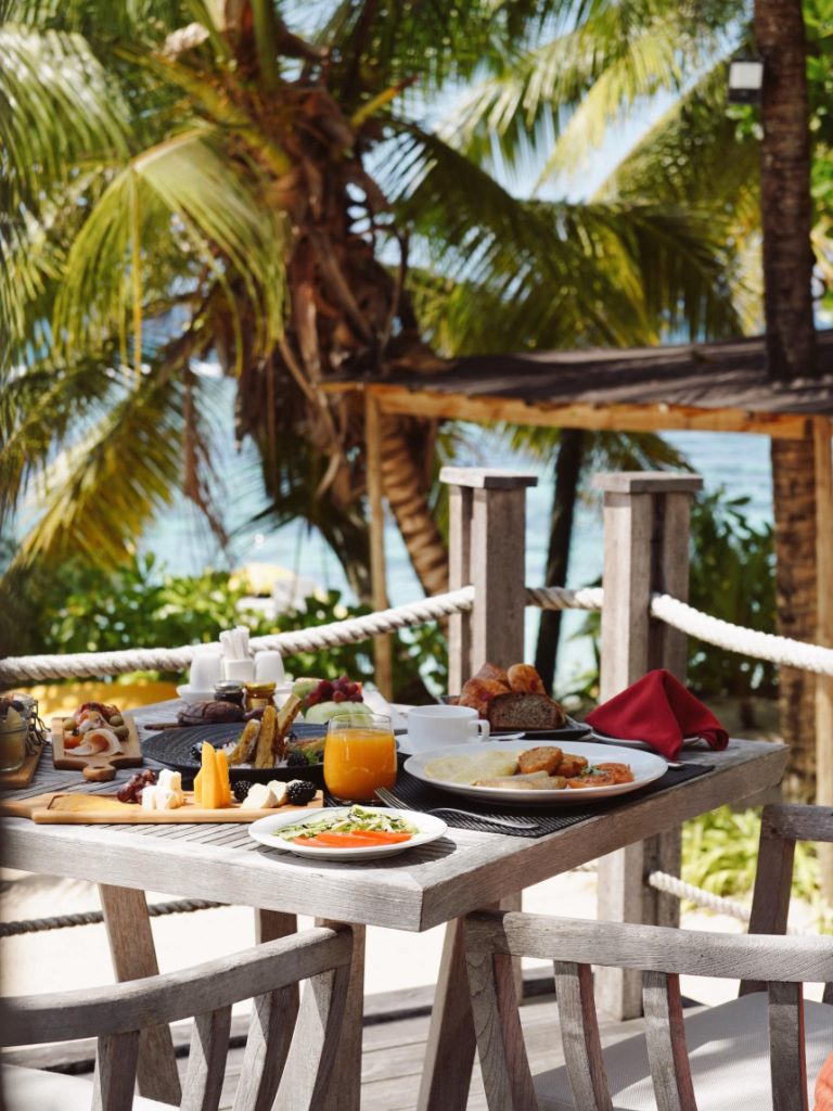 Holztisch mit reichhaltigem Frühstück auf Terrasse mit Meeresblick und Palmen im DoubleTree Allamanda Resort