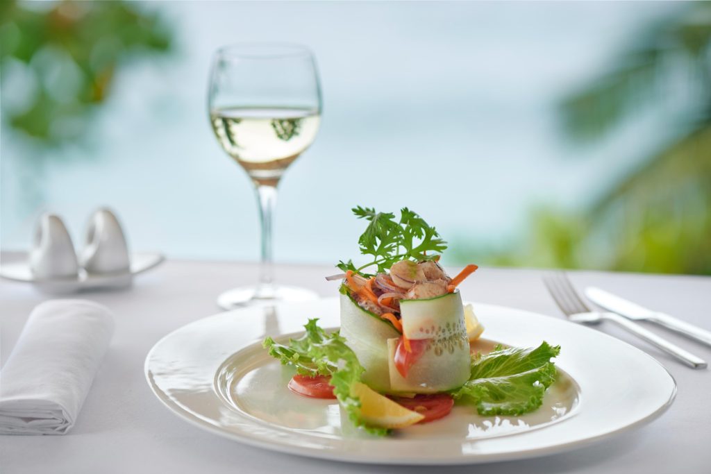 Weiß gedeckter Tisch mit Teller, frischer Gemüsevorspeise, Stoffserviette und Weißweinglas im Restaurant
