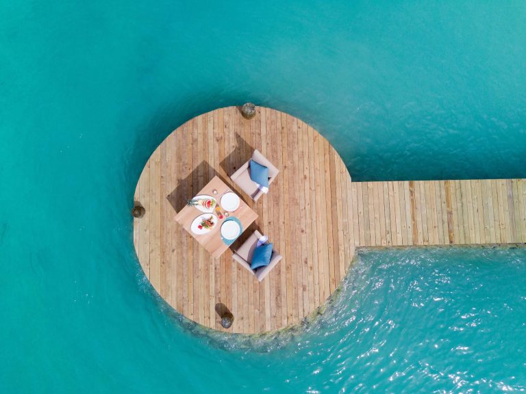 Runde hölzerne Plattform mit Holztisch und zwei Sesseln mit blauen Kissen über türkisblauem Wasser auf den