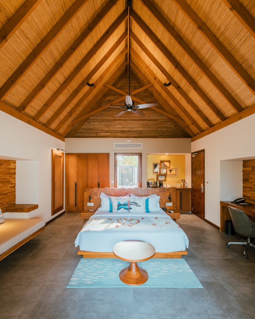 Hotelzimmer im Fushifaru Maldives mit großem Bett, Holzdecke, Steinboden und Tageslicht durch
