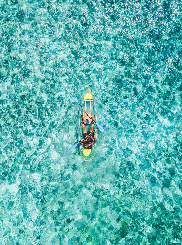 Zwei Personen in transparentem Kajak auf klarem türkisfarbenem Wasser aus der Draufsicht in Fushifaru Maldives
