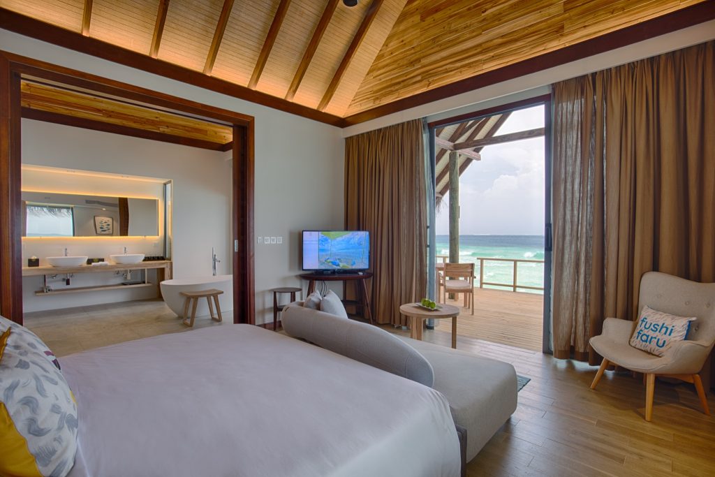 Modernes Hotelzimmer mit großem Bett, Holzfußboden, Badezimmer mit Doppelwaschbecken und Balkon mit Meerblick