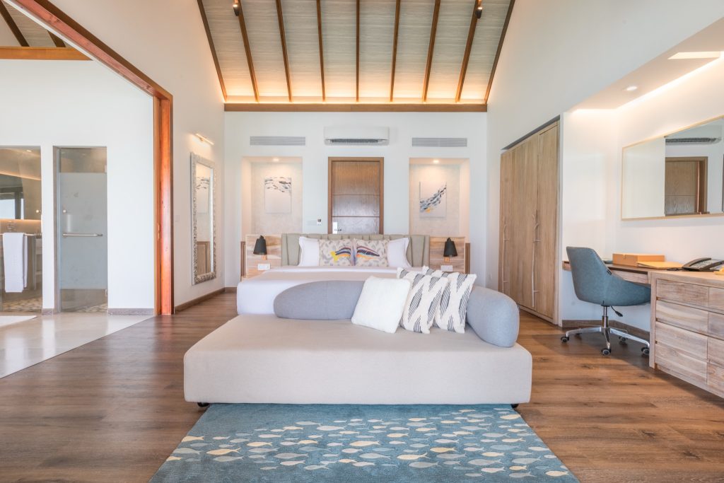 Modernes Hotelzimmer mit großem Bett, weißen Wänden, Holzboden, Holzmöbeln und Tageslicht auf Fushifaru Maldives