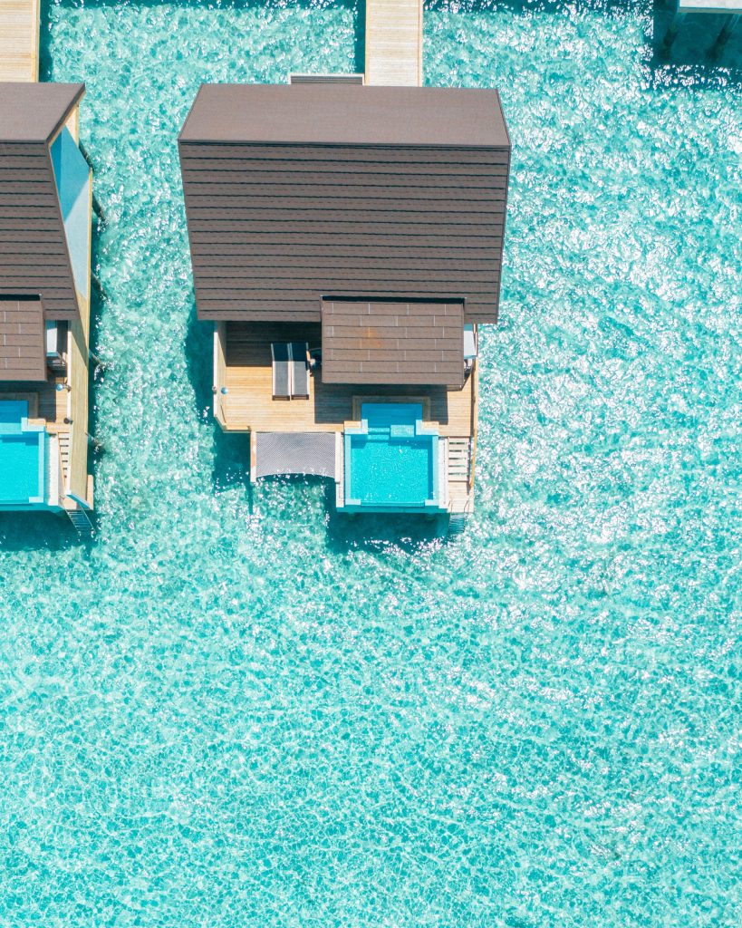Zwei Überwasser-Bungalows mit Holzdecks und privaten Pools auf türkisfarbenem Meer bei hellem Tageslicht