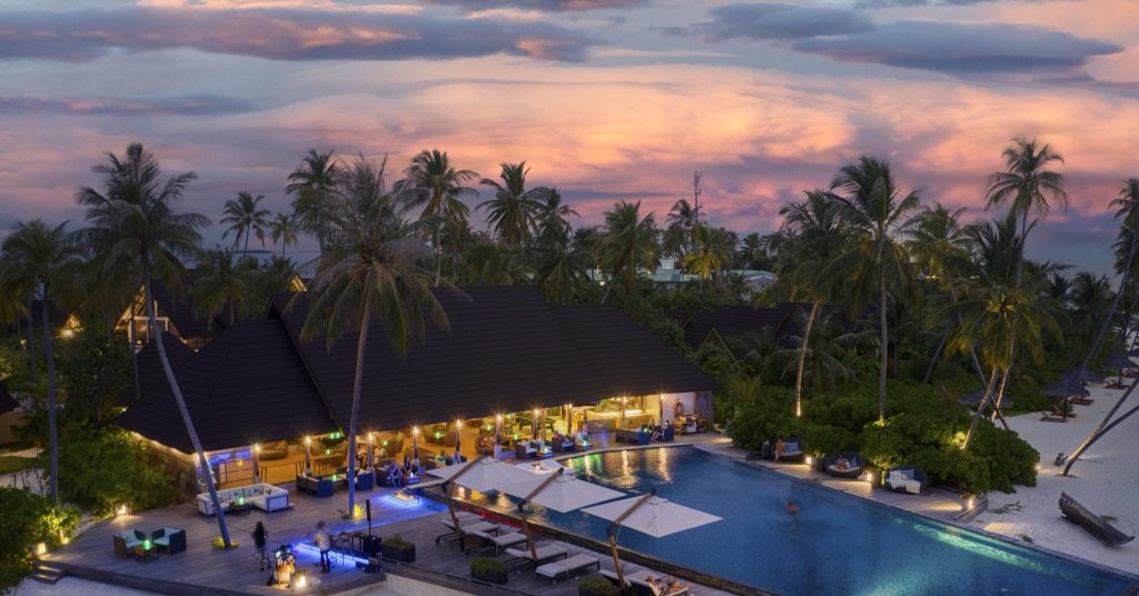 Fushifaru Maldives Restaurant Fanihandhi mit Holzstruktur, großem Pool, Palmen und Strand bei Abendlicht