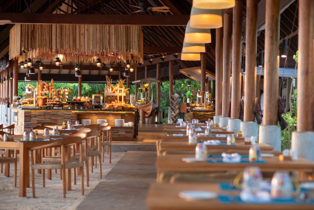 Offenes Restaurant Korakali mit Buffet, Holztischen, Stühlen, Deckenbalken und grünen Pflanzen im Hintergrund