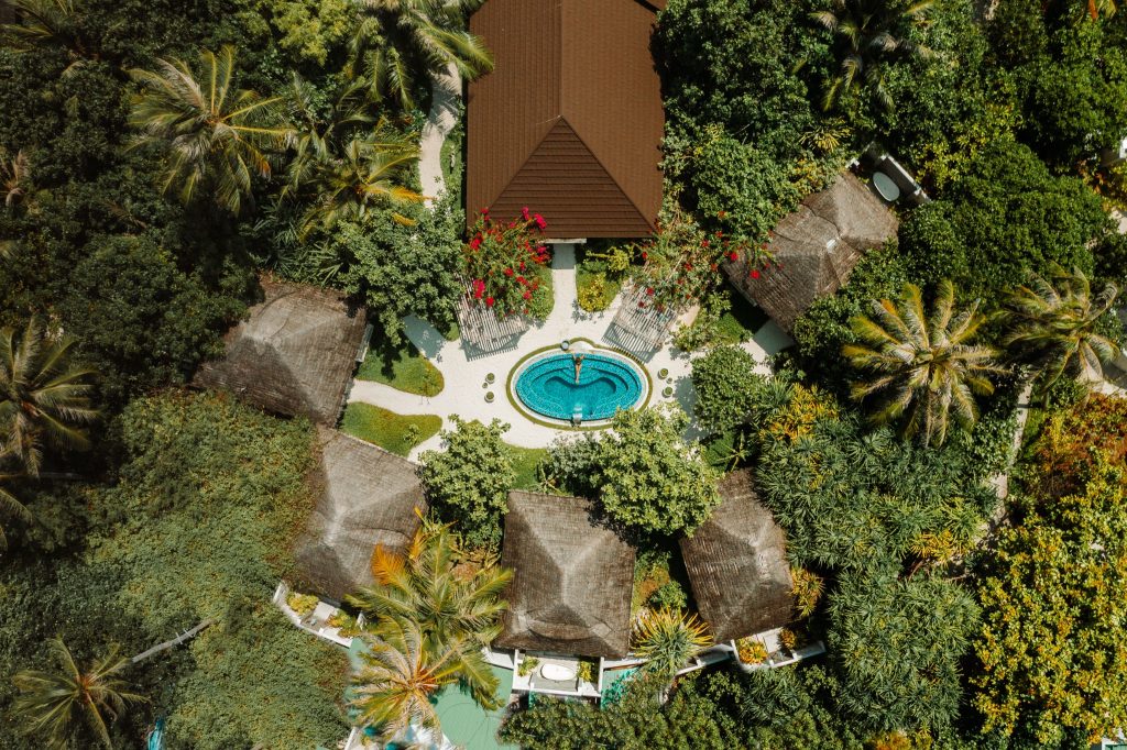 Luftaufnahme des Heylhi Spa mit ovalem Pool, Strohdach-Bungalows und grüner Vegetation im Fushifaru Maldives