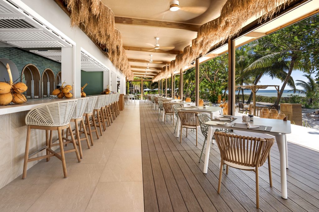 Offener Bar- und Restaurantbereich mit Barhockern, gelben Kokosnüssen, Holz- und Fliesenboden, Palmenblick Seychellen