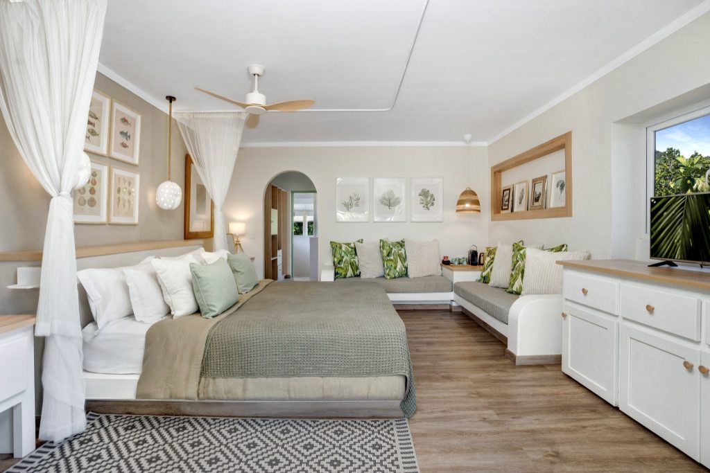 Standard Zimmer der Indian Ocean Lodge mit Doppelbett, weißen und grünen Kissen, Holzfußboden und maritimen Bildern