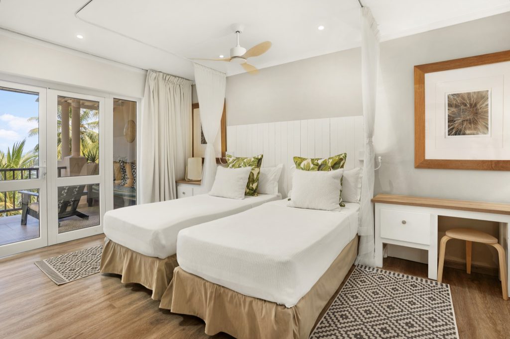 Hotelzimmer Standard Twin mit zwei Einzelbetten, weißen Laken, grünen Kissen und Terrasse mit Palme auf den
