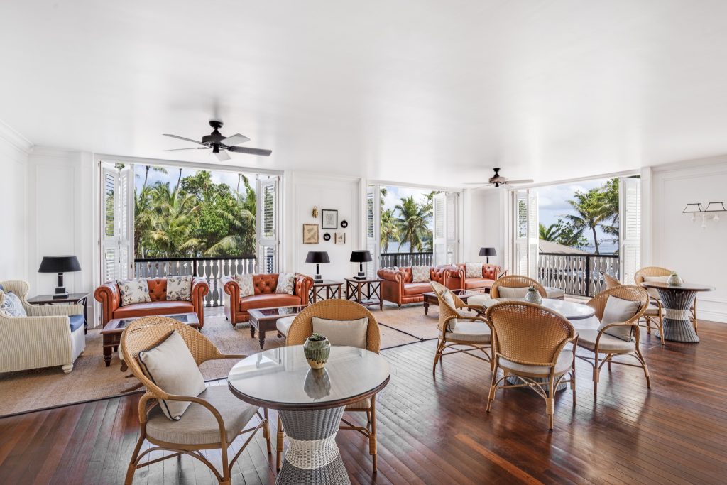 Hotel-Loungebereich Planters Lounge mit braunen Ledersofas, Rattanstühlen und Glastischen mit Blick auf Palmen