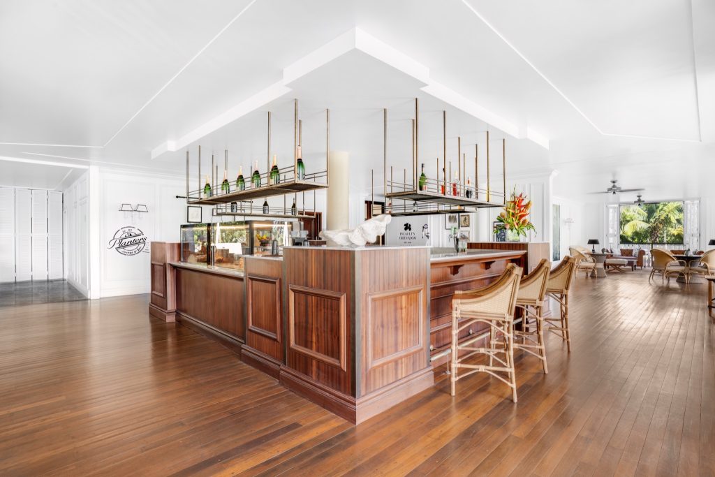 Helle Hotelbar mit Holzboden, dunkler Holztheke und goldfarbenen Regalen mit Flaschen und Gläsern