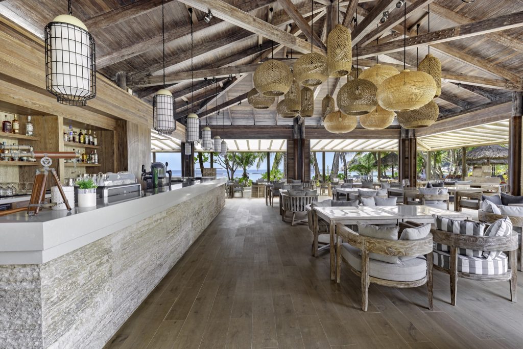 Offene Bar Windsong mit weißem Steintresen, Holzmöbeln und Blick auf Palmen und Meer auf den