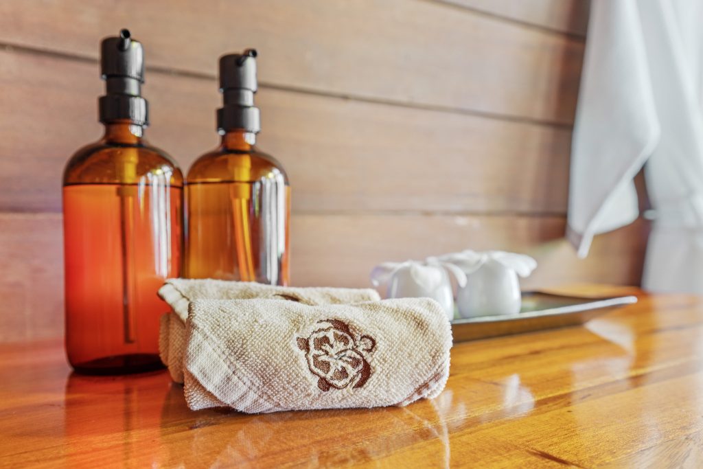 Zwei braune Glas-Seifenspender auf Holzfläche mit besticktem Handtuch und Keramikbehältern im Kempinski Seychelles Resort.