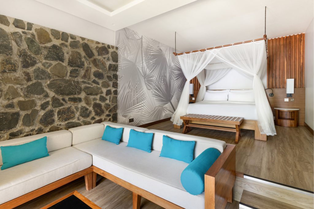 Deluxe Ocean View Garden Room mit Himmelbett, Sitzgruppe, Holz- und Steinwänden im Kempinski Seychelles Resort