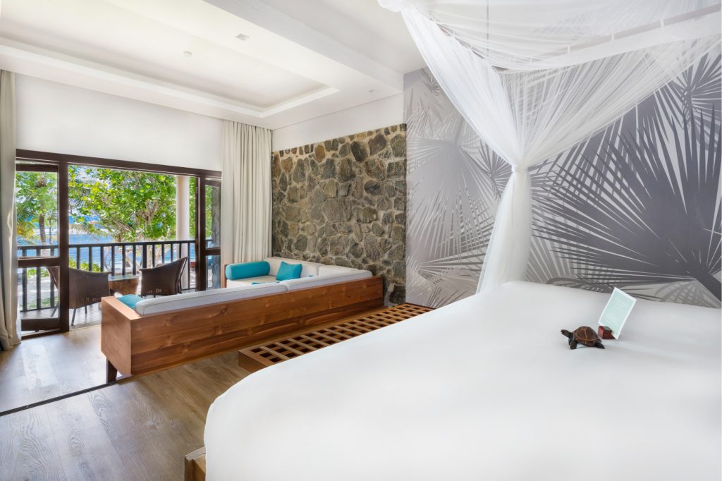 Hell eingerichtetes Deluxe Ocean View Room mit großem Bett, Moskitonetz, Sofa und Meerblick im Kempinski Seychelles Resort