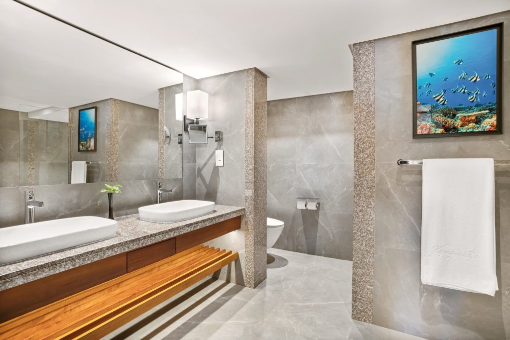 Modernes Badezimmer mit zwei weißen Aufsatzwaschbecken auf grauer Steinplatte und grauer Marmorwand im Kempinski Seychelles.