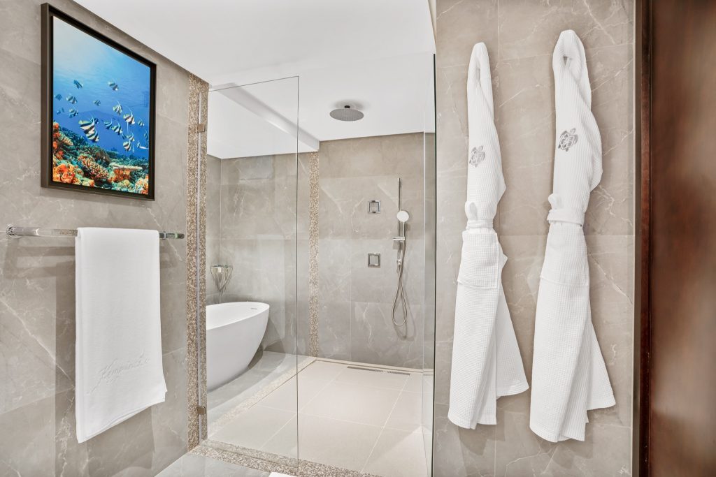 Modernes Badezimmer mit freistehender Badewanne, Glasdusche, beigefarbenem Marmor und Unterwassermotiv im Kempinski.