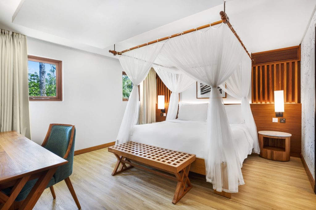 Zimmer der Deluxe Ocean View Suite im Kempinski Seychelles Resort mit Himmelbett, Holzfußboden und tropischem Ausblick