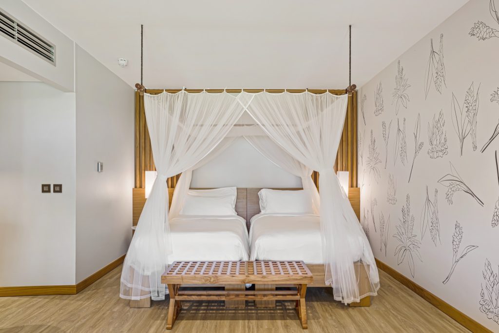 Modernes Family Room im Kempinski Seychelles Resort mit Doppelbett, weißen Vorhängen, Holzfußboden und floralen.
