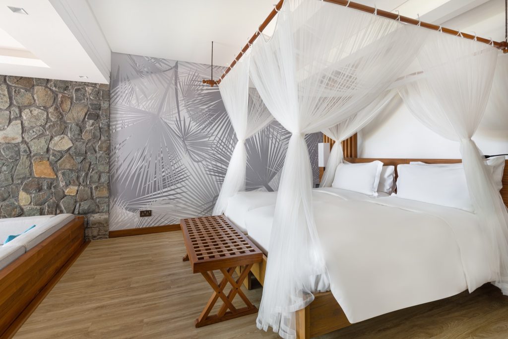 Hotelzimmer Kempinski Seychelles Resort Family Room mit Himmelbett, Holzfußboden und grauer Natursteinwand