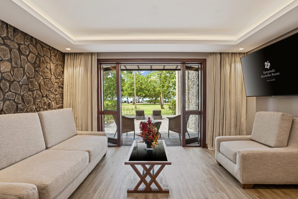 Zimmer der Picault Suite im Kempinski Seychelles Resort mit zwei beigen Sofas, Natursteinwänden und Blick auf Garten