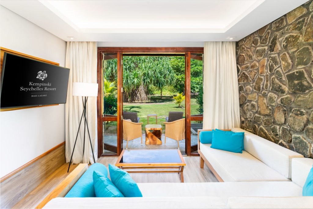 Modern eingerichteter Superior Hill View Room mit Glaswand, weißem Sofa und Steinverkleidung im Kempinski Seychelles Resort