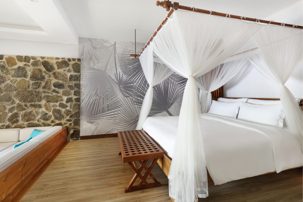 Superior Hill View Room mit Himmelbett, Steinwand, grauer Tapete, Holzboden und Sofa im Kempinski Seychelles Resort
