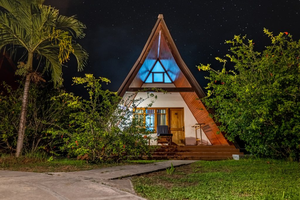 Dreieckiges Garden Chalet aus Holz mit A-förmigem Dach und blau beleuchteten Glasfenstern unter Sternenhimmel