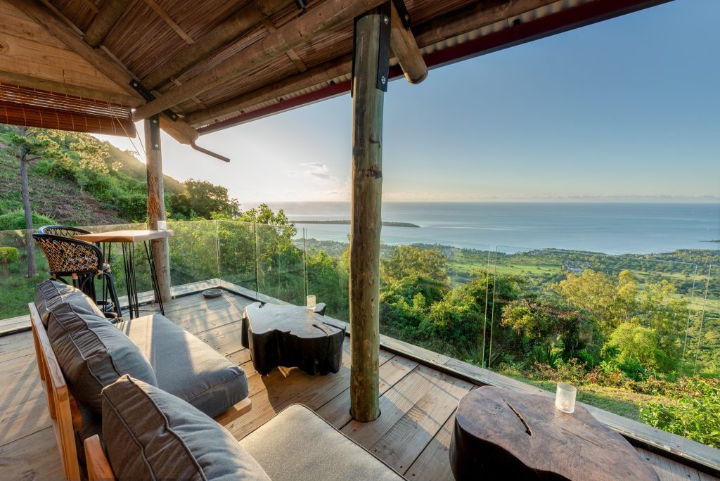 Terrasse der Lakaz Chamarel Exclusive Lodge Bar mit Holzboden, Holzdach, grauer Sitzlounge und Blick auf grüne Landschaft.