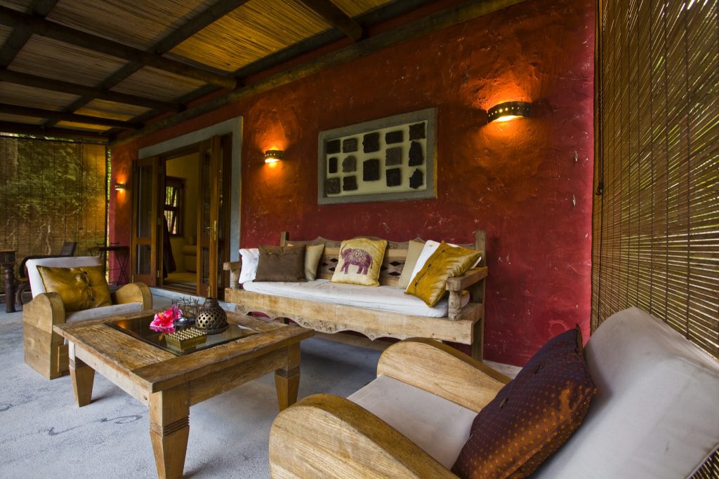 Gemütliche Hotelterrasse mit Holzmöbeln, roten Wänden, Bambusrollo und warmen Wandleuchten in Lakaz Chamarel Exclusive Lodge