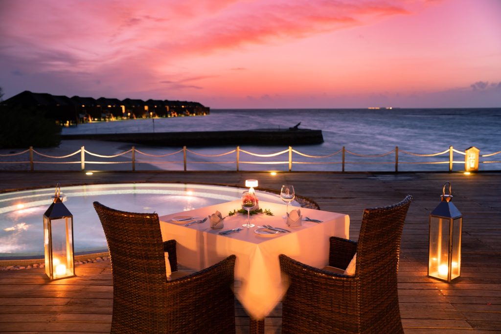 Außenterrasse der Bar Aqva Pool Bar mit gedecktem Tisch, Rattanstühlen und Laternen am Meer