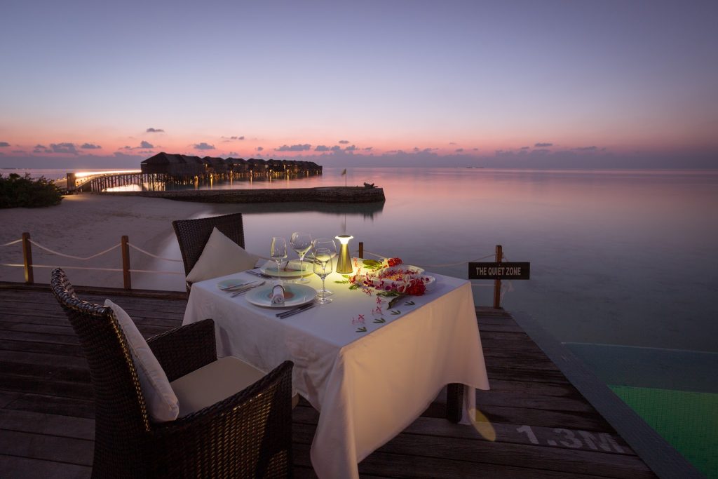 Abendlicher Meerblick mit gedecktem Tisch und über Wasser stehenden Bungalows im Lily Beach Resort & Spa