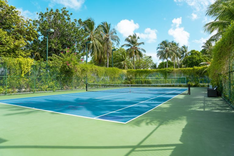 Tennisplatz mit blauen und grünen Spielflächen, umgeben von Palmen und dichtem Grün im Lily Beach Resort & Spa
