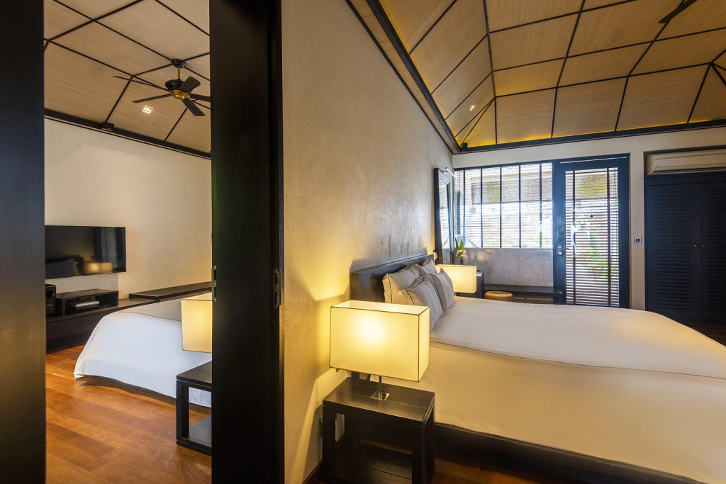 Modernes Hotelzimmer Beach Family Villa mit Schlaf- und Fernsehbereich, dunklen Holzmöbeln und großen Fenstern