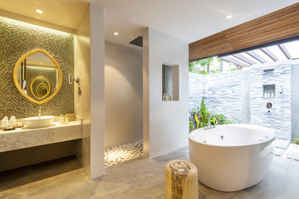 Badezimmer der Beach Residence im Lily Beach Resort & Spa mit Badewanne, Holzverkleidung und rundem Spiegel