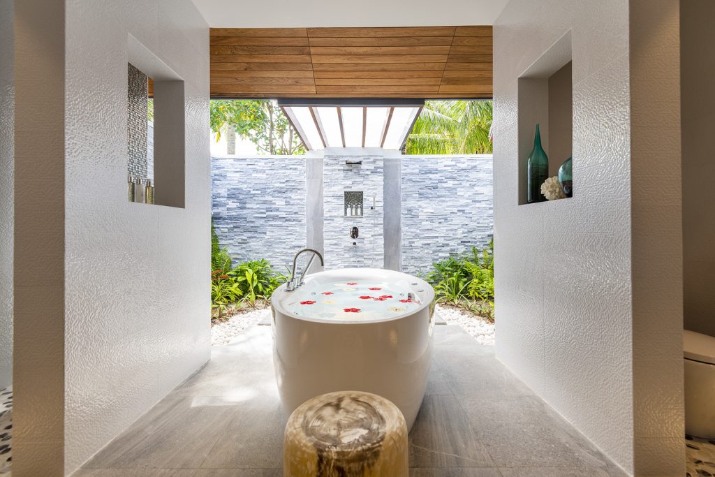 Offenes Badezimmer der Beach Residence im Lily Beach Resort & Spa mit freistehender Badewanne und grauen Steinfliesen