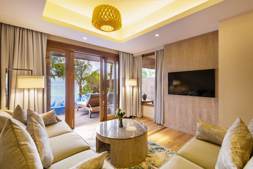 Modernes Hotelzimmer Beach Residence mit Sofa, Holztisch und Zugang zur Terrasse mit Liegestühlen und Pool auf den