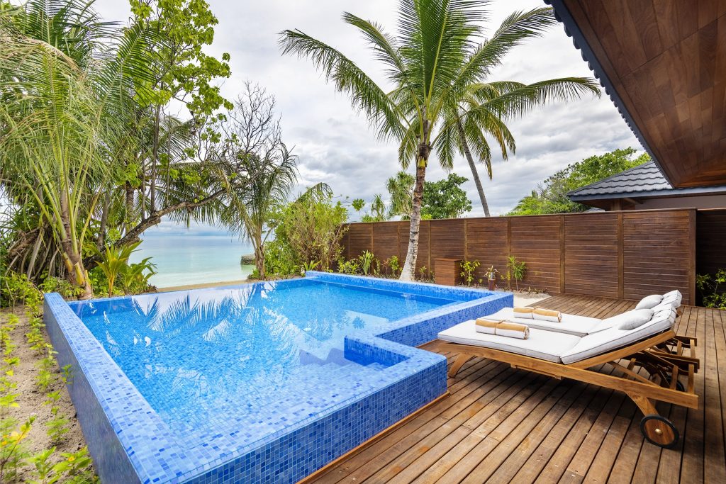 Rechteckiger Swimmingpool mit blauen Mosaikfliesen, Holzdeck, Doppel-Liege und tropischen Pflanzen in der Beach Residence