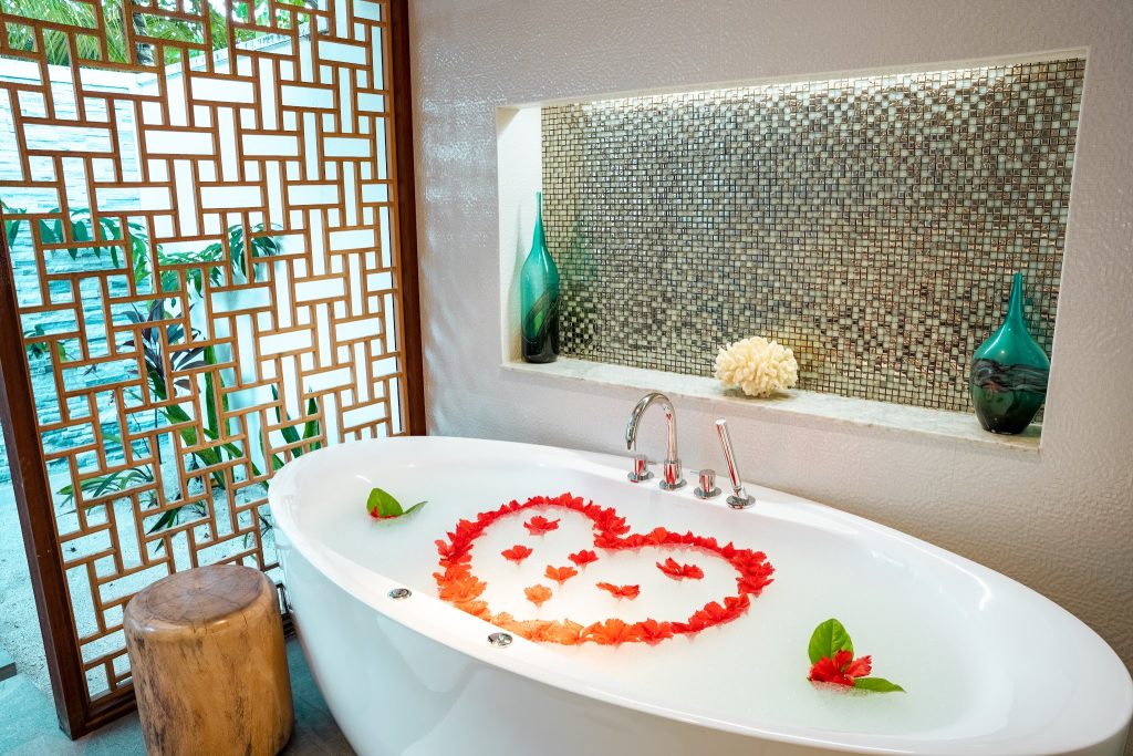 Badezimmer der Beach Residence mit freistehender Badewanne, roten Blütenblättern und Mosaikwand auf den