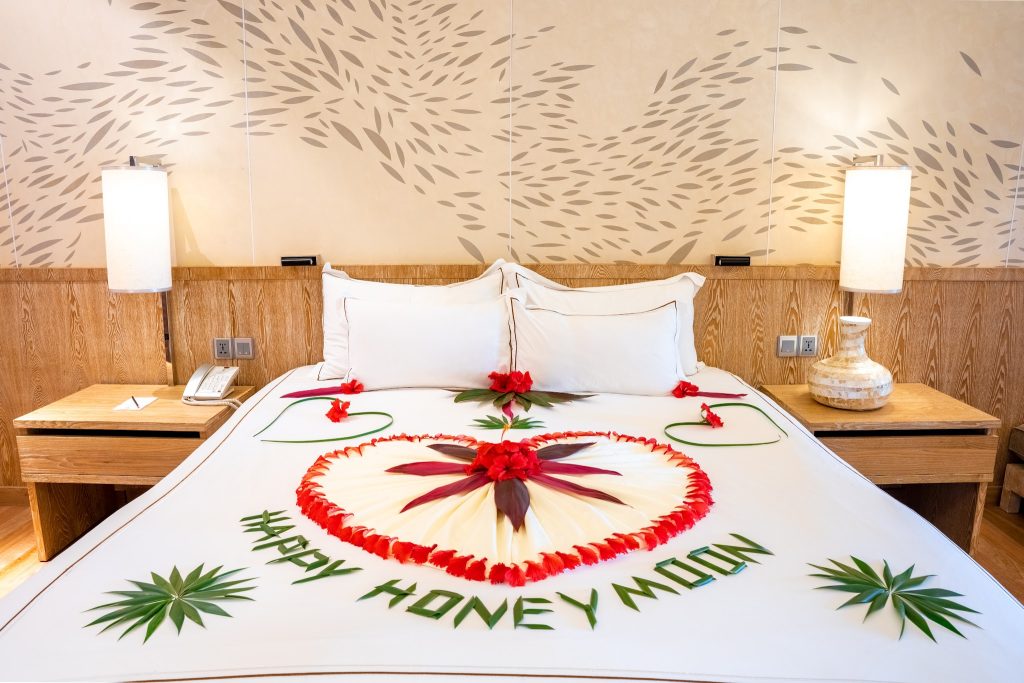 Hotelzimmer Beach Residence mit großem Doppelbett, weißer Bettwäsche und roten Blüten in Herzform.