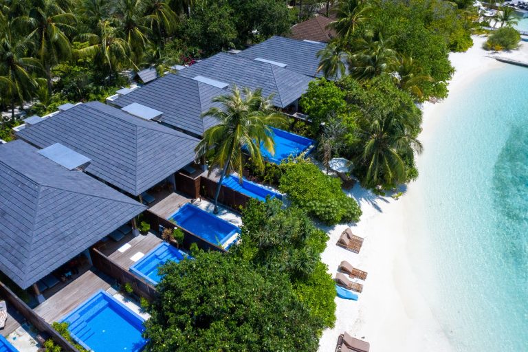 Reihe von Bungalows mit blauen Dächern, privaten Pools und Holzterrassen an weißem Sandstrand auf den