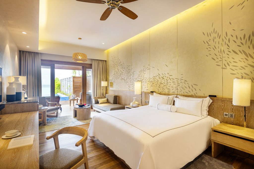 Geräumiges Hotelzimmer Beach Suite mit großem Bett, Holzmöbeln und Zugang zur Terrasse im Lily Beach Resort & Spa