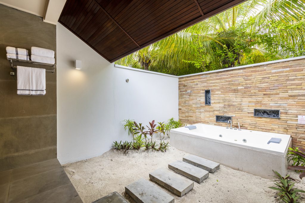 Badezimmer der Beach Villa mit freistehender Badewanne, weißen Wänden, Natursteinwand