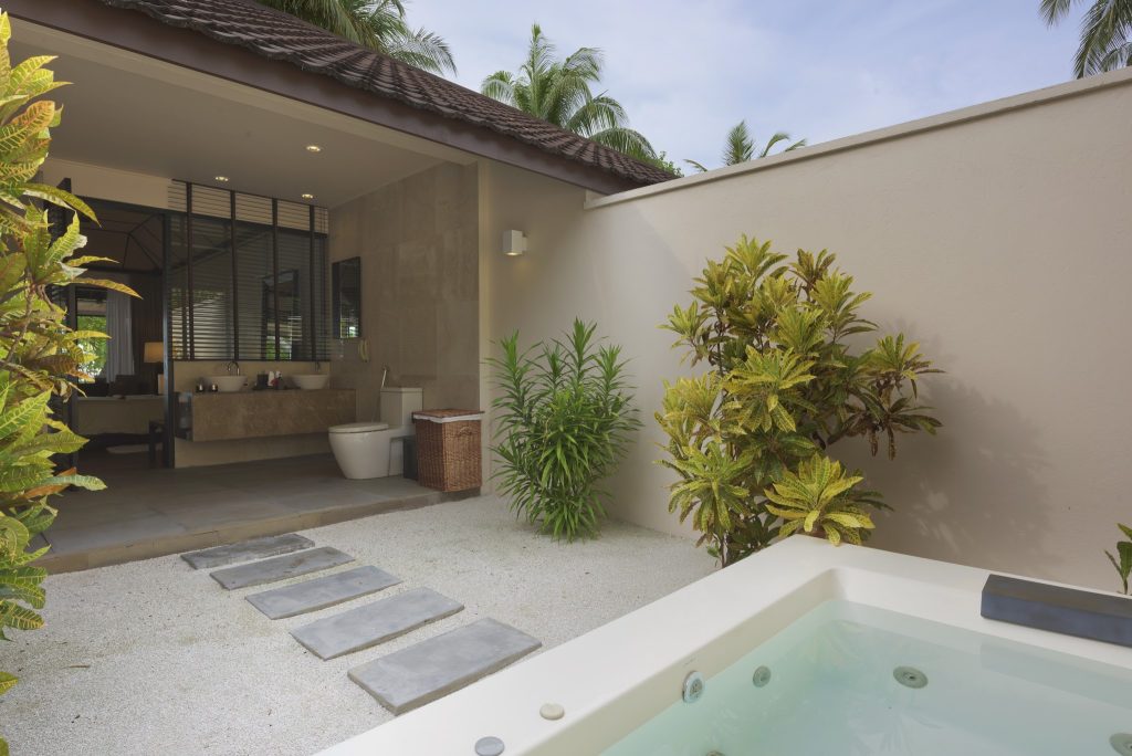 Badezimmer mit zwei Steinwaschbecken, Toilette, großem Spiegel und privatem Außenbereich mit Whirlpool und tropischen.