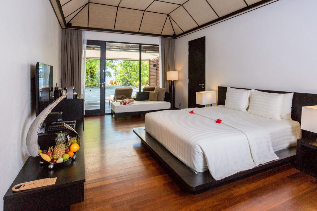 Hotelzimmer Beach Villa mit großem Doppelbett, weißer Bettwäsche, Holzboden und Terrasse mit Liegestühlen auf den
