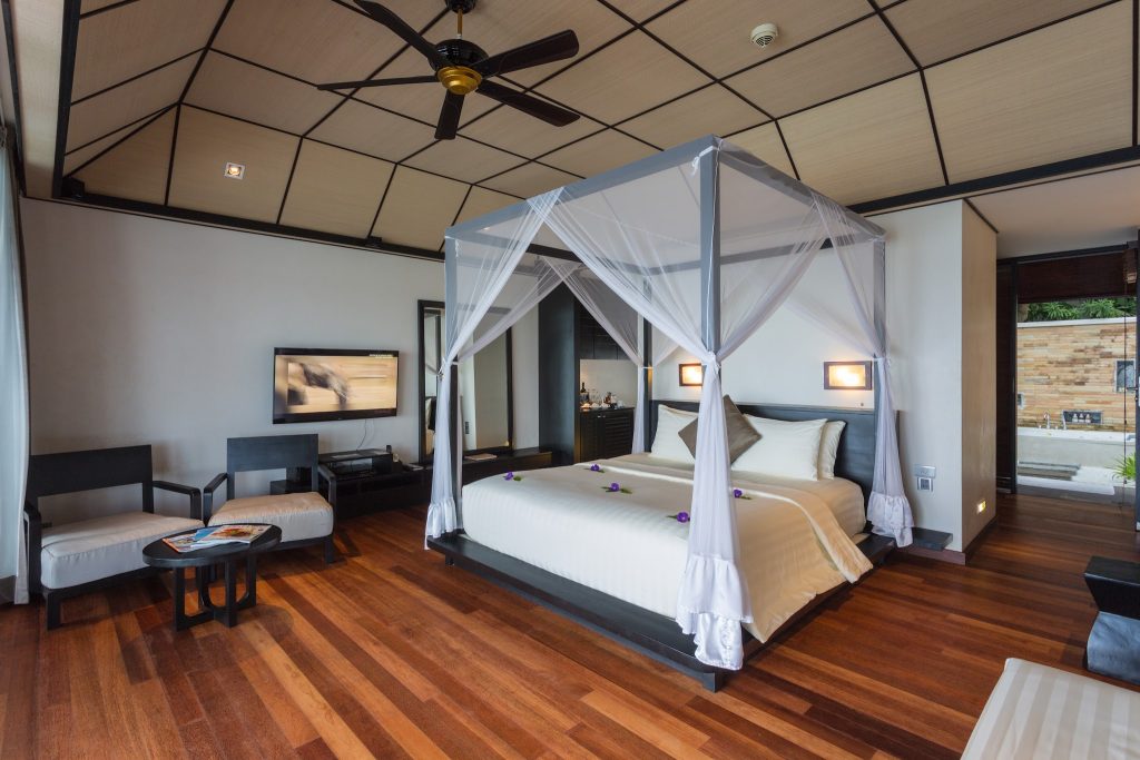 Zimmer der Lagoon Villa im Lily Beach Resort & Spa mit Himmelbett, Holzfußboden und Glastür zum Außenbereich