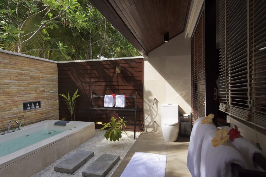 Offenes Badezimmer der Lagoon Villa mit eingelassener Badewanne, Holz- und Steinwänden und tropischem Grün im Hintergrund