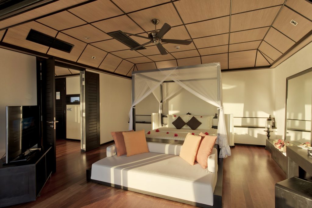 Zimmer der Sunset Water Suite im Lily Beach Resort & Spa mit Holzboden, Himmelbett und weißem Sofa