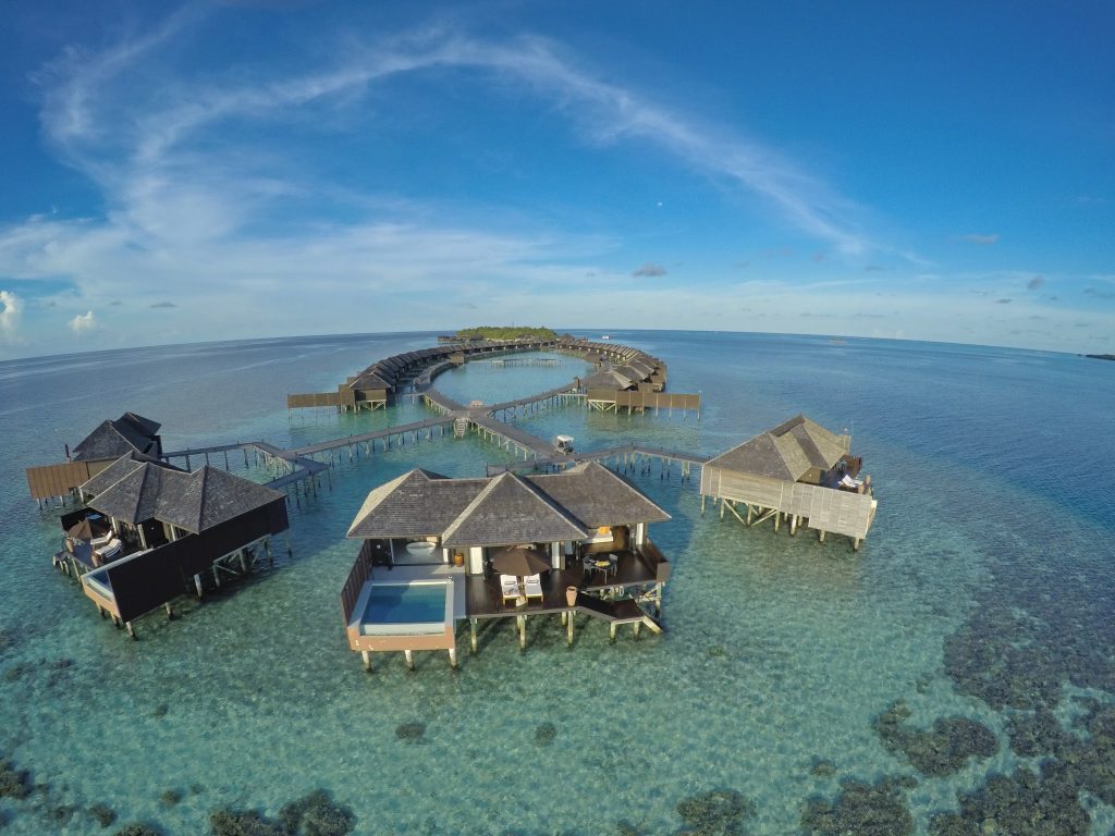 Holzbungalows auf Stelzen mit Strohdächern über türkisfarbener Lagune und Steg im Lily Beach Resort & Spa